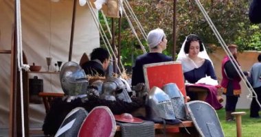 Eski ortaçağ kostümlü kızlar çadıra zırh ve kalkanların yanına yeni savaş üniformaları dikiyorlar.