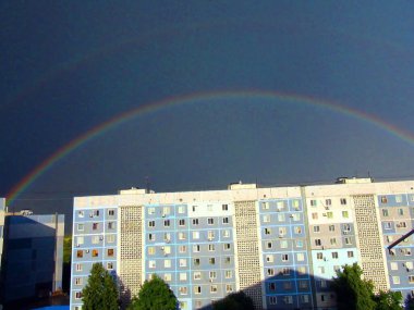 Çok renkli bir gökkuşağı, yaz güneşinin delen ışınları altında yağmur bulutlarının arka planında gökyüzü köprüsü oluşturur..