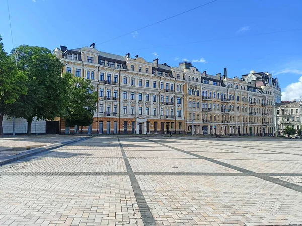 Panorama of ancient medieval buildings surrounding a clean wide square in the center of Kyiv on a sunny summer day.
