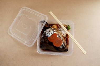 Soya soslu haşlanmış somon balığı kafası (somon kabutonisi) eve götürmek için kare plastik kutu ve kahverengi ahşap arka plan.