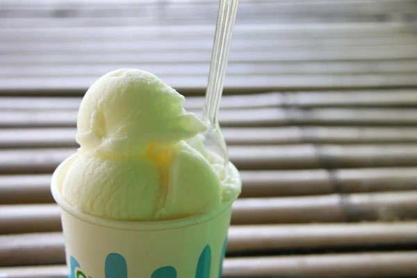 White ice cream made from goat milk in paper cup with small plastic spoon and blur bamboo background, Thailand.