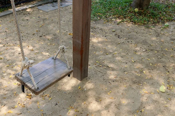A wood swing is hanging over ground beside wood pole, Thailand.