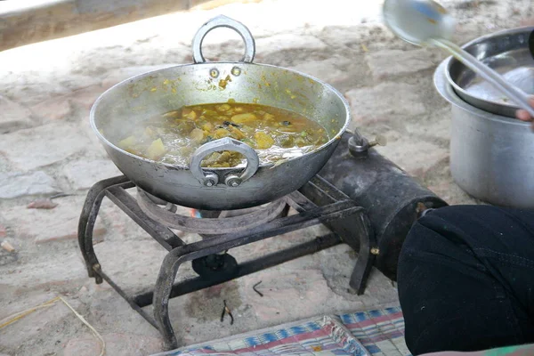 Iron pan on portable stove cooking Indian food in trip, India. Curry in pan boiling.