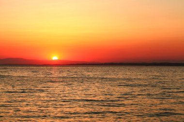 Deniz tarafından gün batımı, gökyüzü denize yansıyor.