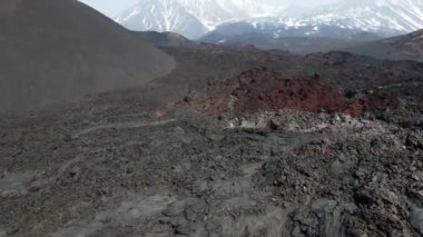 Karla kaplı volkanlara tepeden bakan donmuş siyah lav.