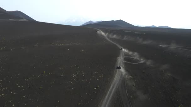 Coches conducen en la tierra negra con vistas a los volcanes — Vídeo de stock