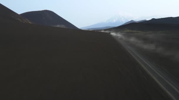 Cars drive on black earth overlooking volcanoes — стоковое видео