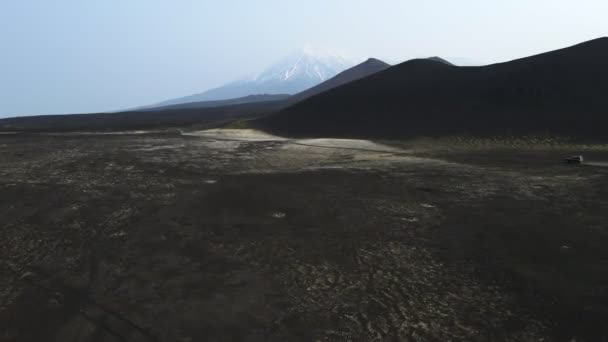Autos fahren über schwarze Erde mit Blick auf Vulkane — Stockvideo