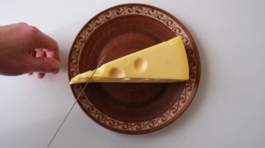 a large piece of cheese lies on a ceramic plate, man cuts a small piece 