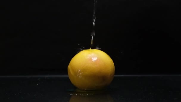 Orange on a black background on which a stream of water pours — Stock Video
