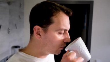 a man drinking pensively from a white cup at home in the kitchen