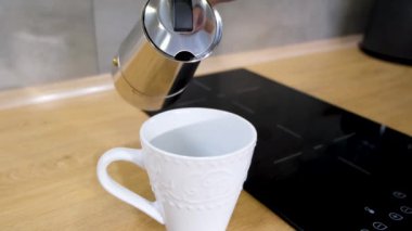 a man at home in the kitchen pours coffee from a coffee maker into a white cup