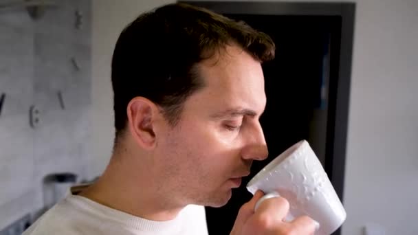 Чоловік п'є з білої чашки вдома на кухні — стокове відео