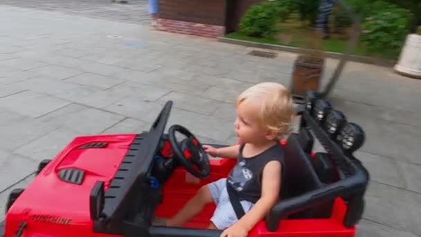 Mały chłopiec blondynka jedzie sam w dla dzieci elektryczny samochód — Wideo stockowe