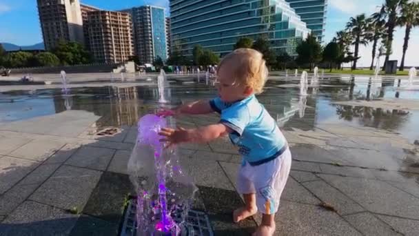 Liten pojke blond blöter händerna i fontänen — Stockvideo