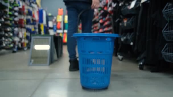 Мужчина делает покупки в спортивном магазине, ходит с тележкой, кладет в нее товар — стоковое видео