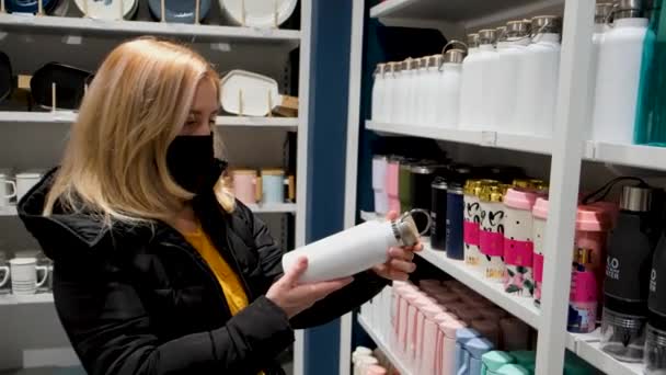 Una mujer en una máscara elige un producto en una tienda de vajilla — Vídeos de Stock