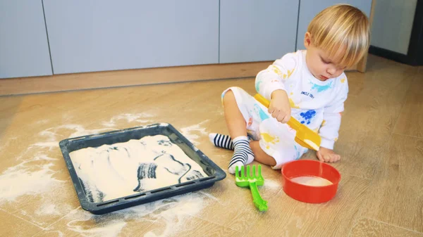 Uma criança pequena brinca com farinha na cozinha leva farinha com uma pá como se em uma caixa de areia — Fotografia de Stock