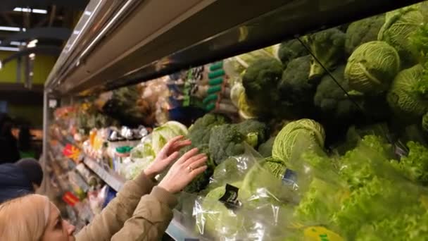 Ein Mädchen in der Gemüseabteilung eines Supermarktes nimmt eine Pumpe Brocoly — Stockvideo
