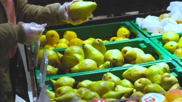 Uma menina no departamento de frutas de um supermercado escolhe grandes peras verdes — Vídeo de Stock