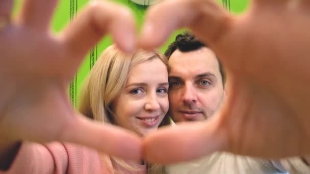 Женщина и влюбленный мужчина сделали сердце из пальцев и посмотрели через него в камеру — стоковое видео