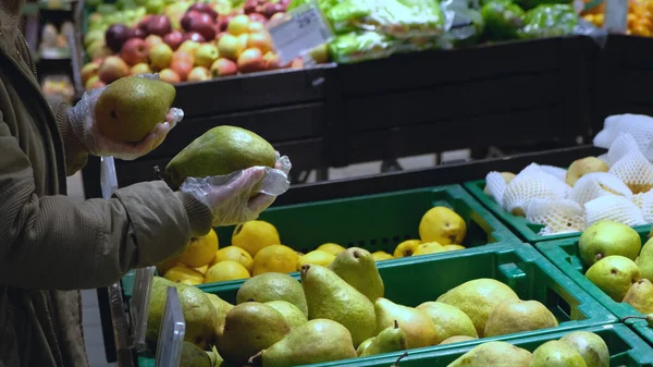 Uma menina no departamento de frutas de um supermercado escolhe grandes peras verdes — Fotografia de Stock