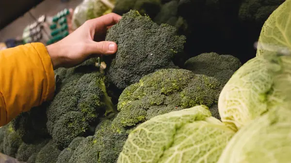 Süpermarketin sebze reyonunda erkek eller brokoli pompası alır. — Stok fotoğraf
