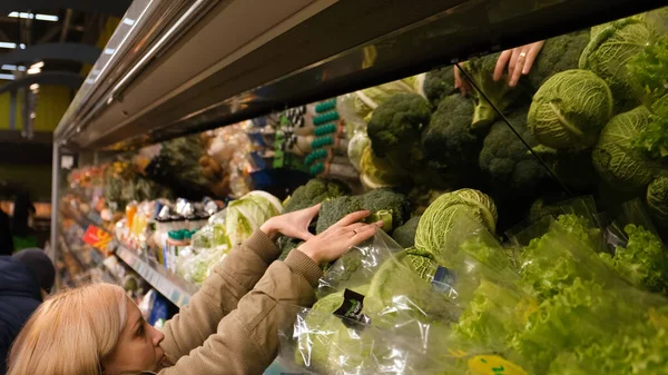 Uma menina no departamento de vegetais de um supermercado leva uma bomba de brocoly — Fotografia de Stock
