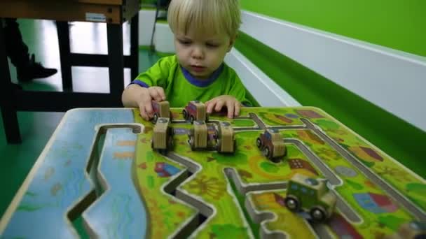 Menino pequeno com um rosto sério brinca com carros de madeira sozinho — Vídeo de Stock