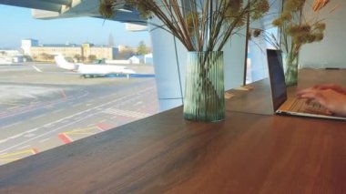 Havaalanındaki genç bir adam havaalanında uçmayı beklerken dizüstü bilgisayarıyla çalışıyor.