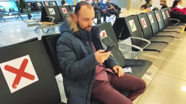 Een man op het vliegveld zit in de wachtkamer leest een bericht aan de telefoon en springt vrolijk uit de stoel — Stockvideo