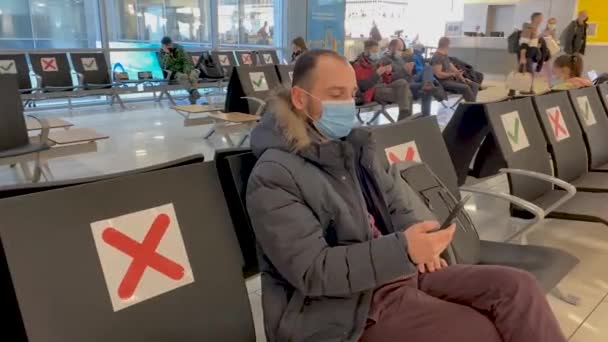 Un homme masqué à l'aéroport est assis dans la salle d'attente lit un message au téléphone et saute joyeusement de la chaise — Video