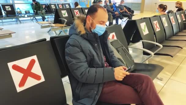 空港のマスクの男が待合室に座って電話でメッセージを読んで喜んで椅子から飛び上がる — ストック動画