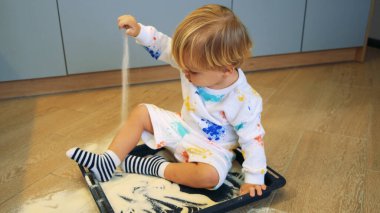 Küçük bir çocuk mutfakta un ile kum gibi oynuyor.