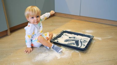 Küçük bir çocuk mutfakta un ile kum gibi oynuyor.