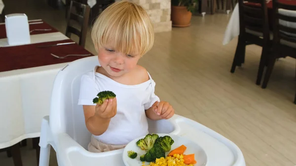 A little boy sits in a highchair and eats vegetables — Fotografia de Stock