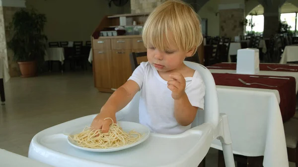 Baby boy eats spaghetti sitting in a baby chair in restaurant — Foto de Stock