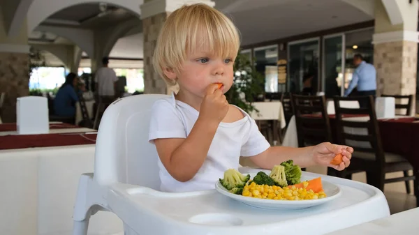 A little boy sits in a highchair and eats vegetables — Fotografia de Stock