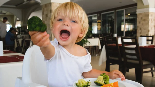 Little boy holds broccoli in his hand and stretches forward — Fotografia de Stock