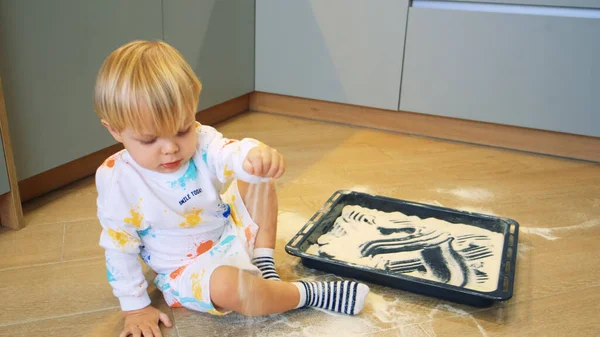 Uma criança pequena brinca com farinha na cozinha como areia — Fotografia de Stock