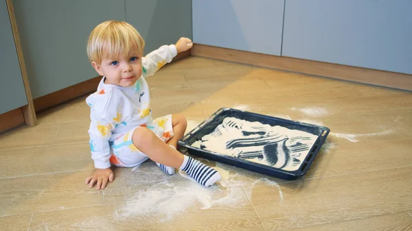 Küçük bir çocuk mutfakta un ile kum gibi oynuyor.