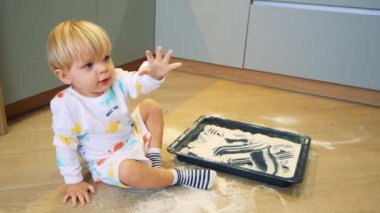 Küçük bir çocuk mutfakta un ile kum gibi oynuyor.