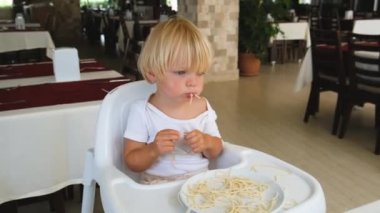 Bebek restoranda bebek sandalyesinde oturmuş spagetti yiyor.