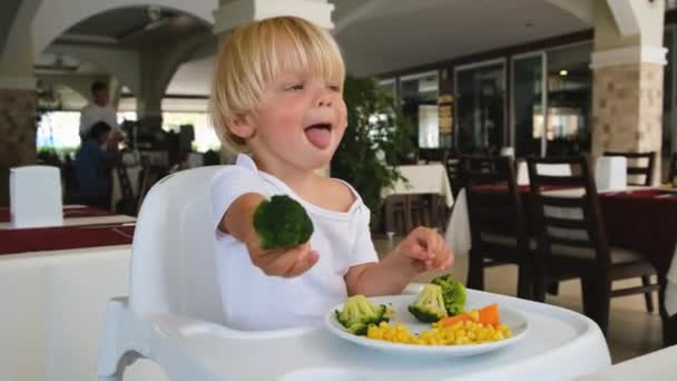 Маленький хлопчик тримає броколі в руці і тягнеться вперед — стокове відео