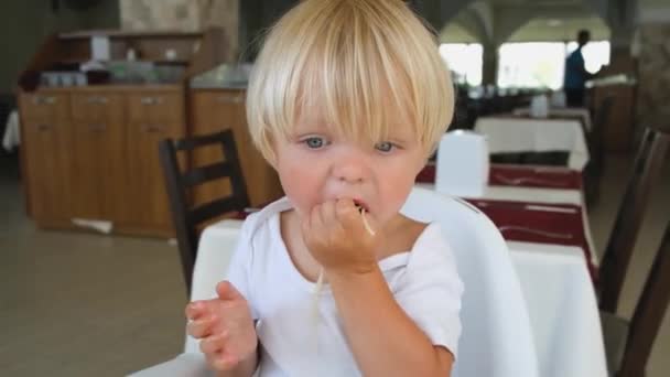 Baby boy eats spaghetti sitting in a baby chair in restaurant — Stock Video