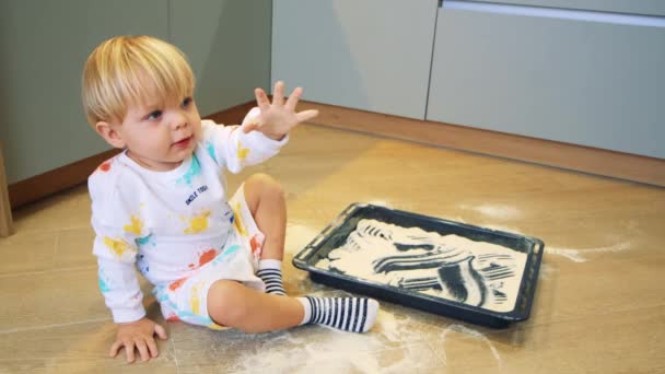 A small child plays with flour in the kitchen like sand — Stock Video