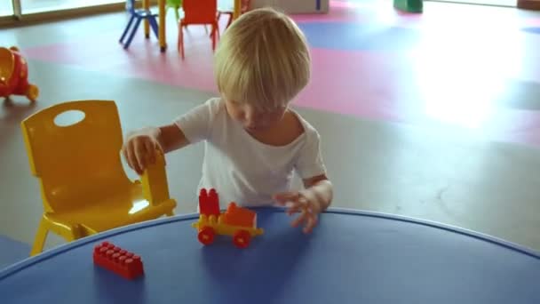 Un niño pequeño juega con un conjunto de construcción sobre la mesa — Vídeo de stock