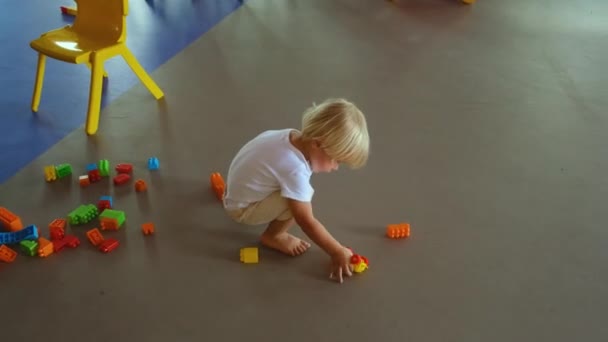 Ett litet barn leker med en byggsats och en leksaksbil på golvet — Stockvideo