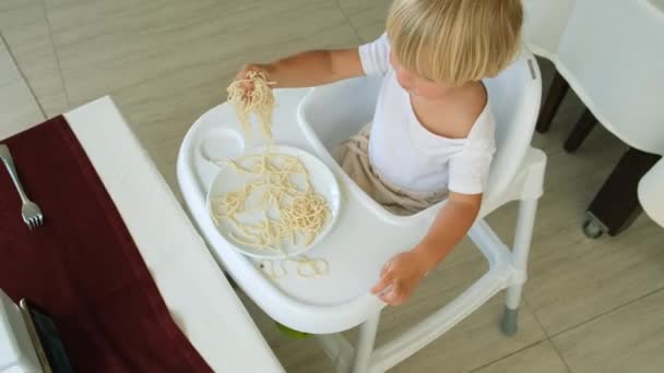 Малыш ест спагетти, сидя в детском кресле в ресторане — стоковое видео