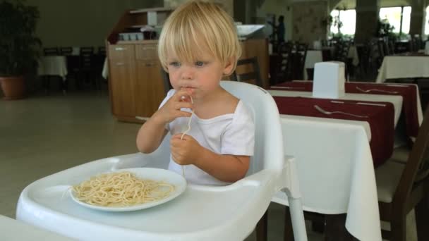 Baby boy eats spaghetti sitting in a baby chair in restaurant — Stok video